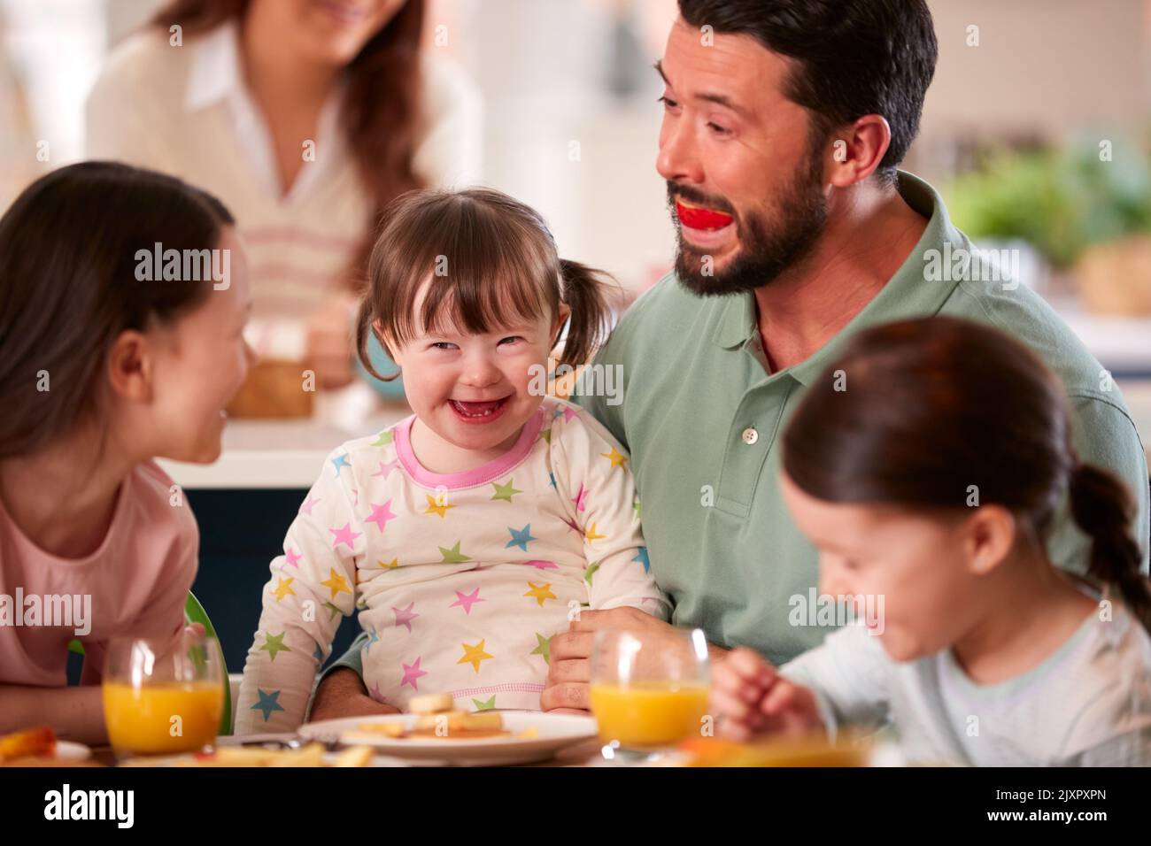 Father Making Funny Face As Family With Down Syndrome Daughter Eat Breakfast At Home Stock Photo