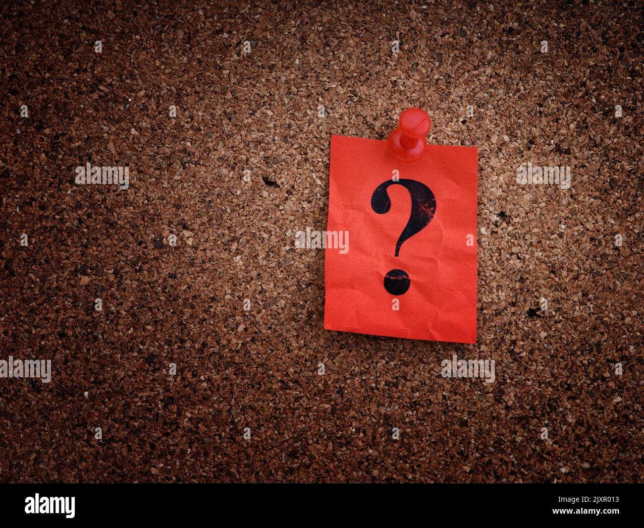 A red paper note with a question mark on it pinned to a cork board. Close up. Stock Photo