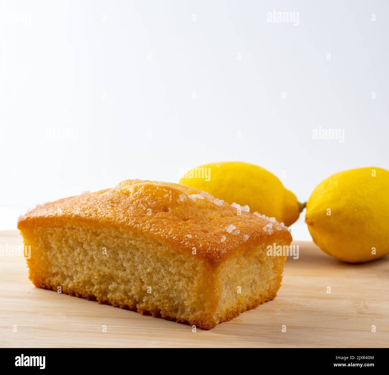 Lemon drizzle cake  and fresh lemons on a bamboo board with white background Stock Photo