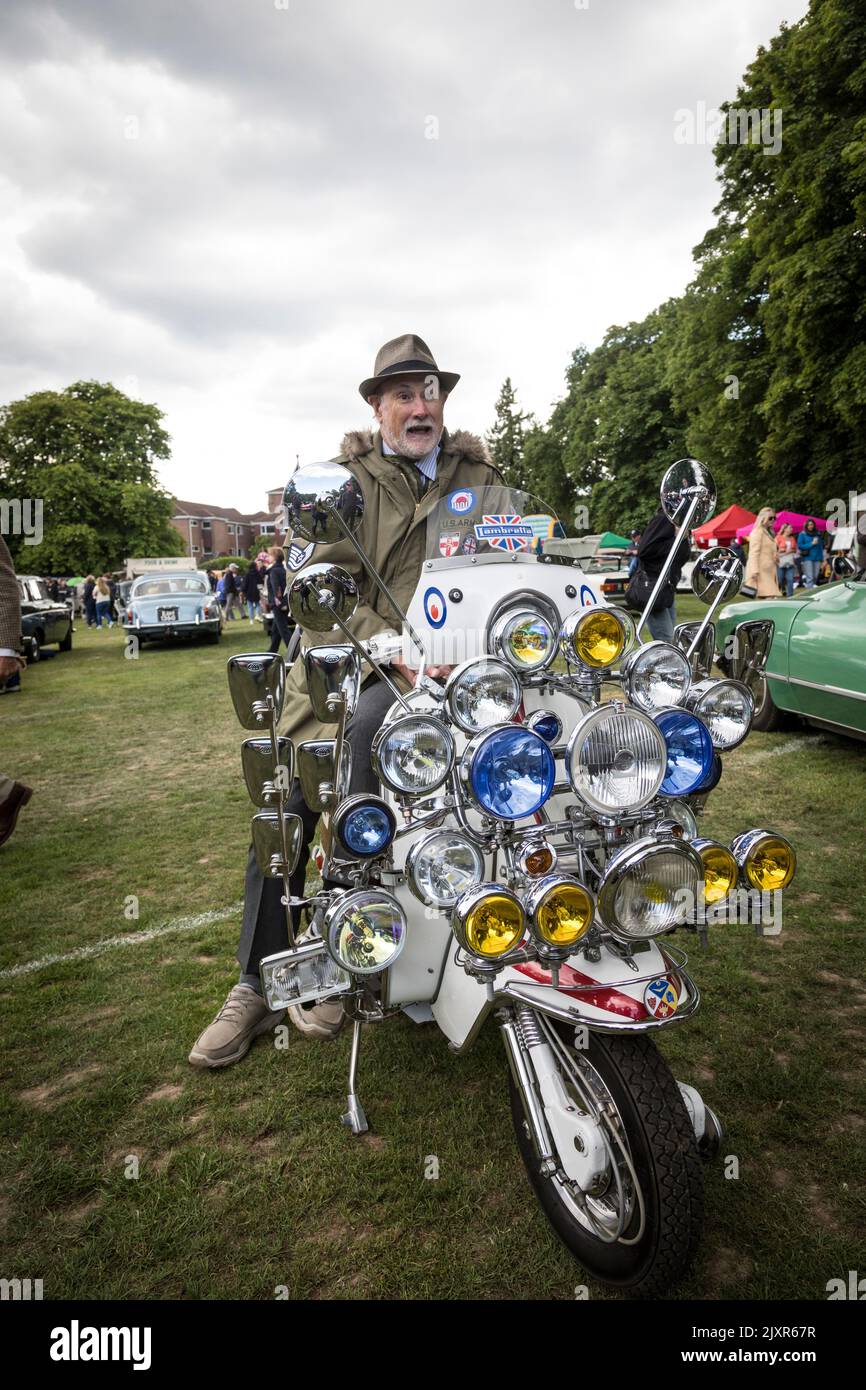 Man sits astride his vintage Lambretta scooter complete with numerous lights and mirrors, at a classic car rally, Haslemere, England. Stock Photo