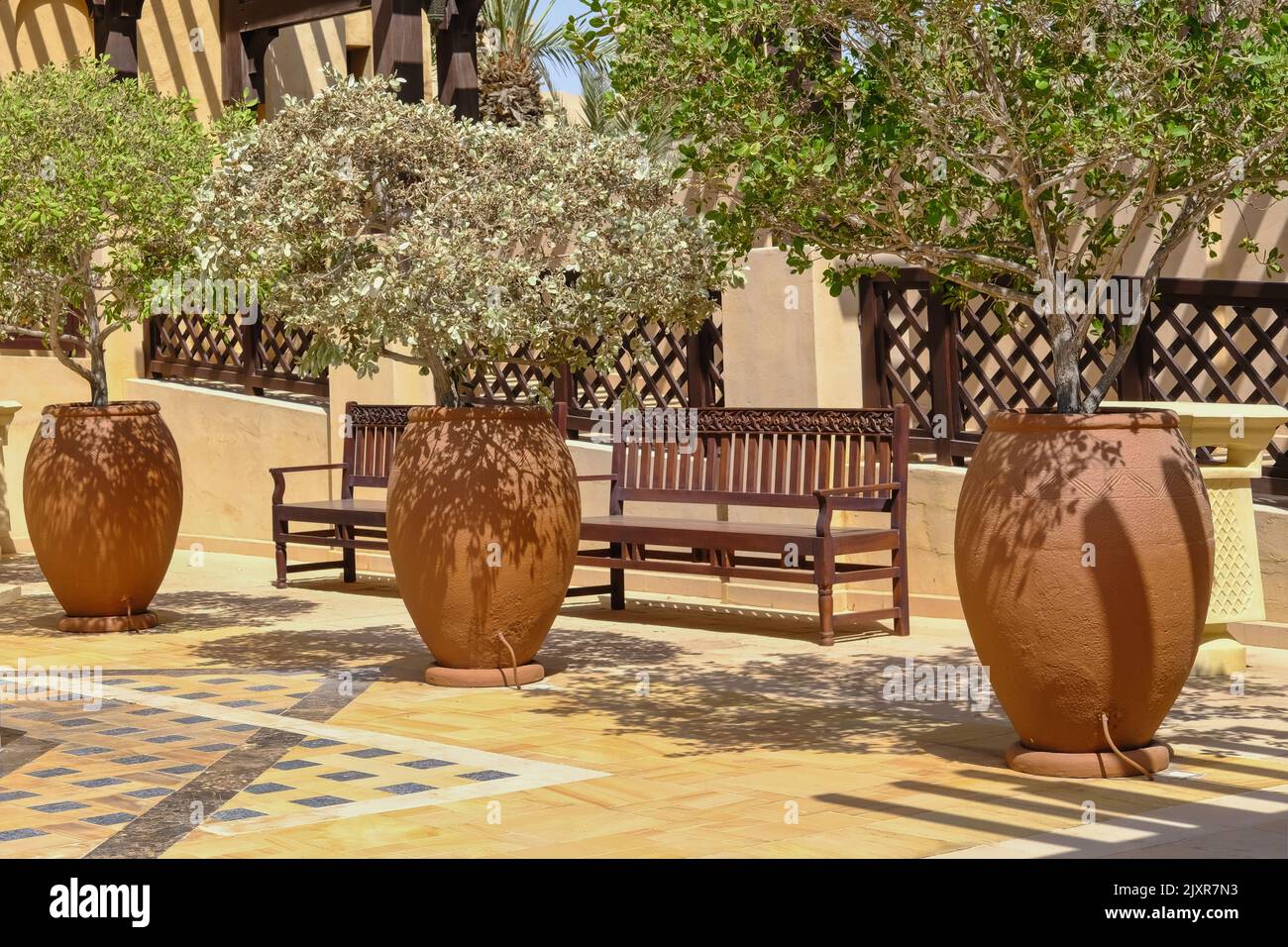 Orient ceramic floor vases with plants and wooden benches with carved arabesque floral pattern in courtyard of middle eastern villa or palace. Stock Photo