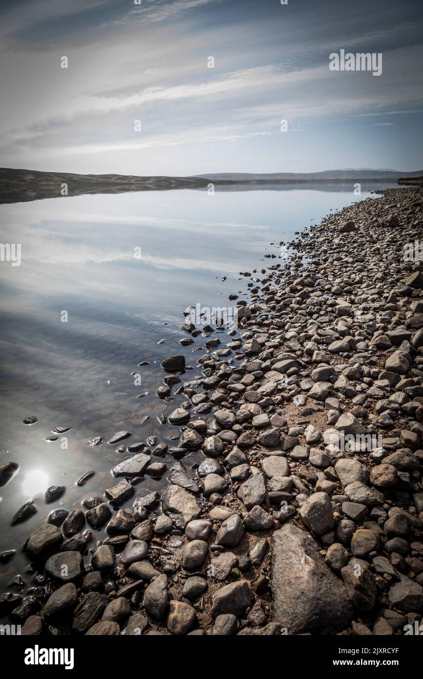 With its rocky shoreline, clouds and sky are reflected in the still clear water of Loch Loyal, Scotland. Stock Photo