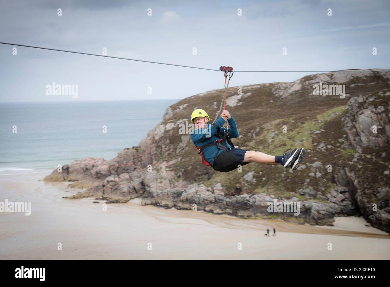 Man enjoying a zip wire ride above Ceannabeinne Beach, Scotland. Stock Photo