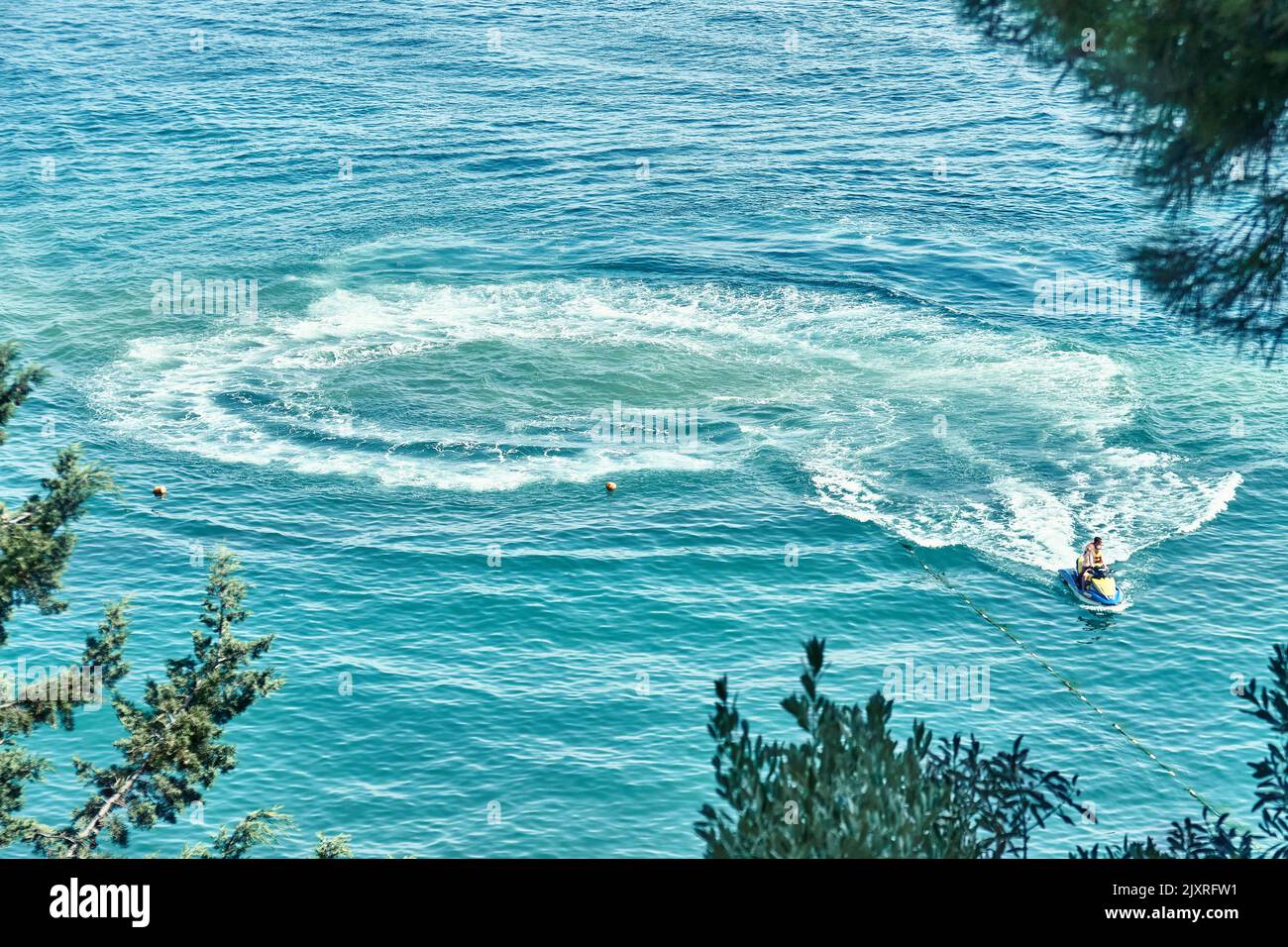 Huge trace waves on sea left by tourist riding jet ski. Person wearing life jacket makes circles from waves on water enjoying extreme sports Stock Photo