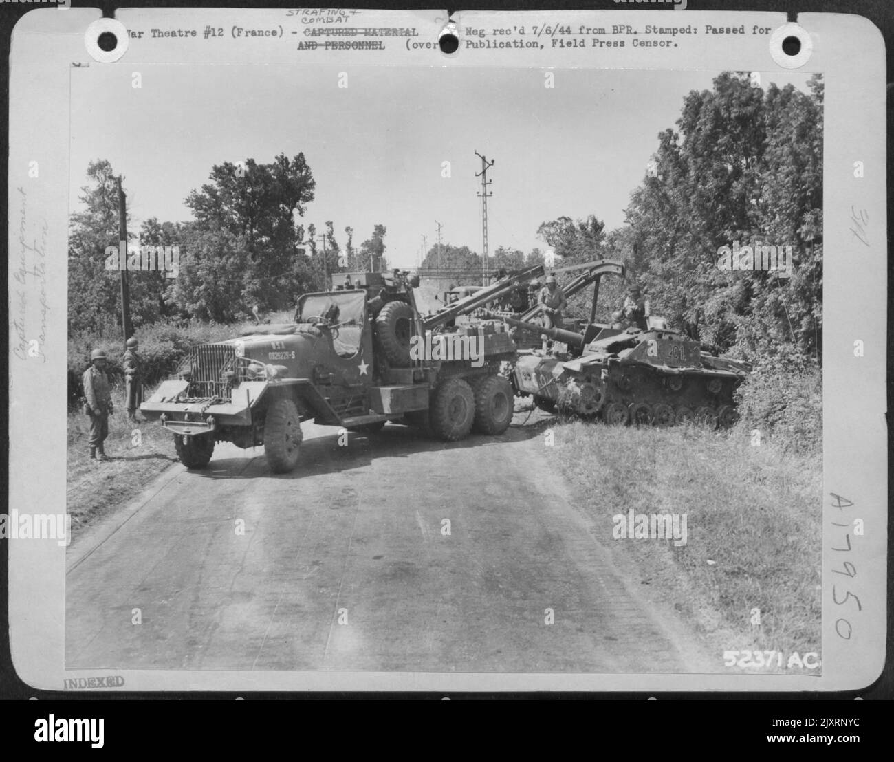 Members of the Ninth Air Service Command are shown towing a disabled Nazi tank from a ditch where it was abandoned by the enemy. Stock Photo