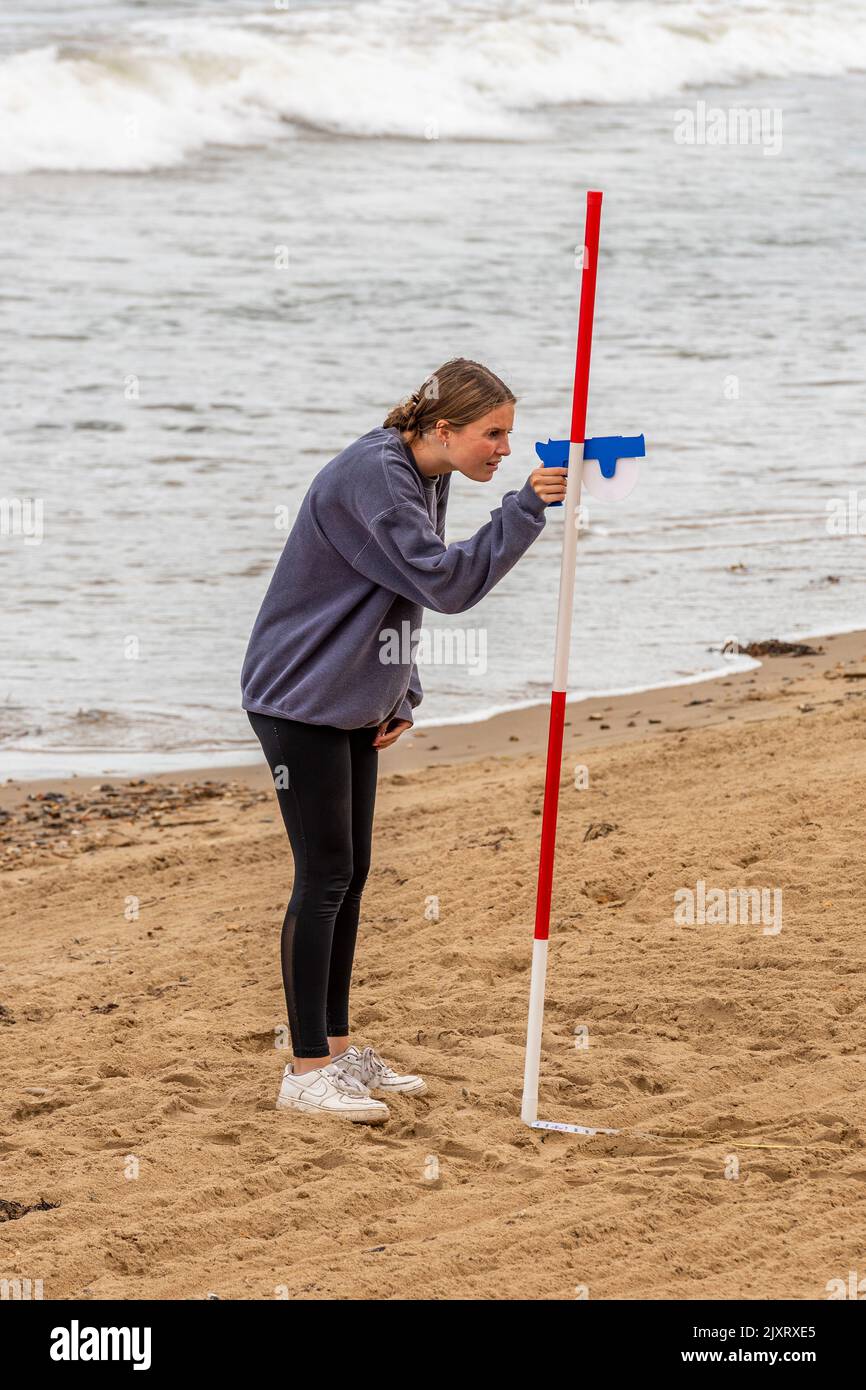 young woman carrying out a survey using pole and theodolite on a beach in dorset, surveying a beach with specialist survey equipment, pole and gun. Stock Photo