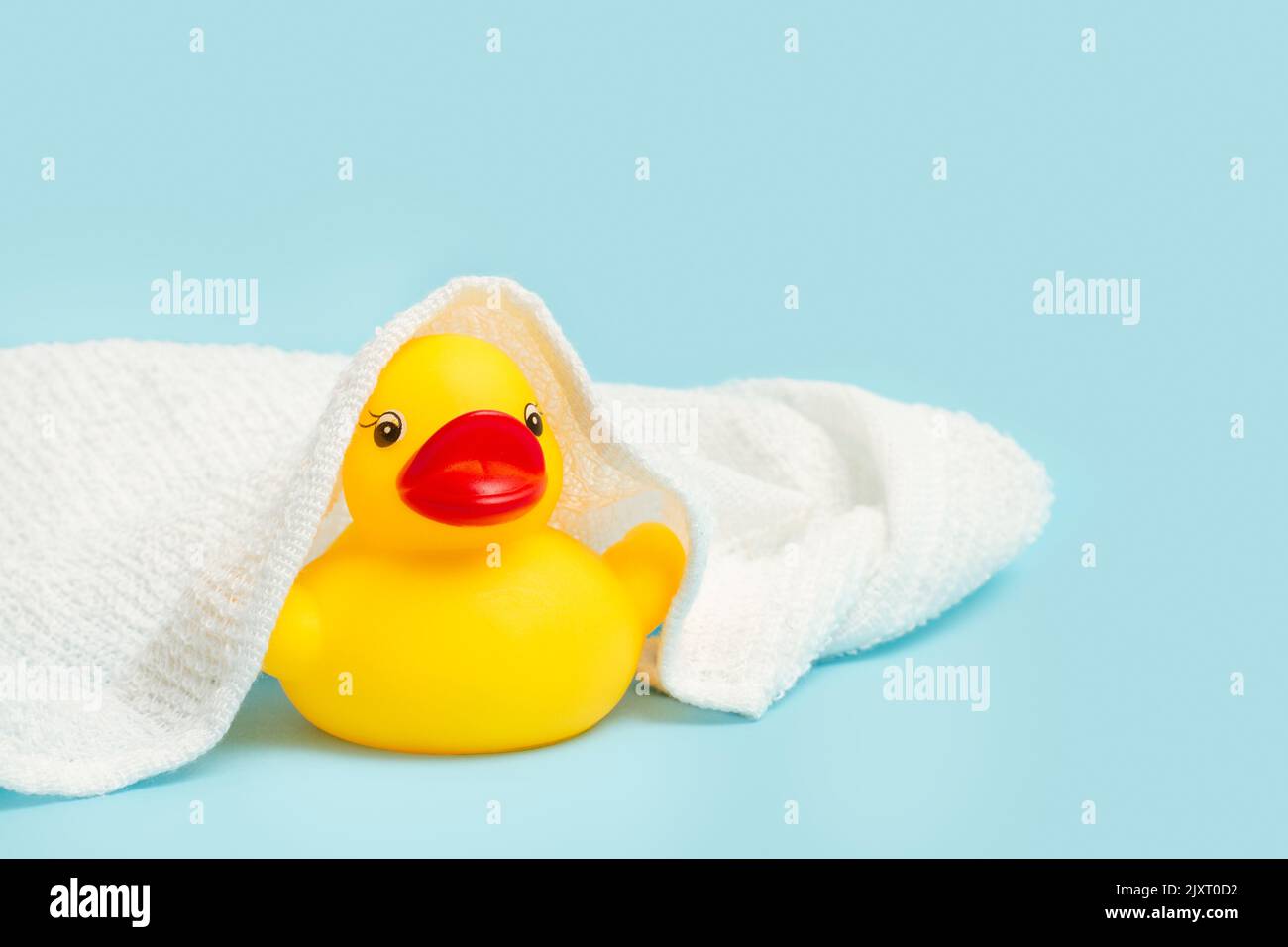 A yellow rubber toy duck with a towel over him and on a light blue ...