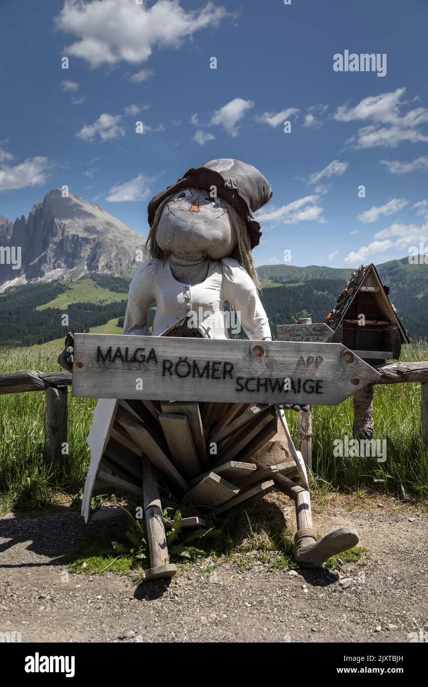 A rustic stuffed figure holds a sign to a nearby property on a path in the Italian Dolomites. Stock Photo