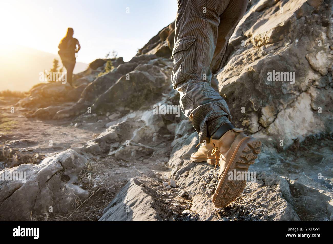 Closeup photo of male hiker legs and blurred female tourist with backpack walking at trail Stock Photo