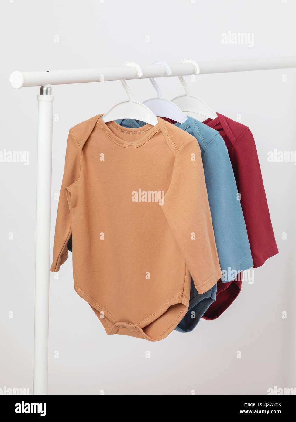 Baby overalls with long sleeves on a hanger, baby bodysuits in three colors Stock Photo