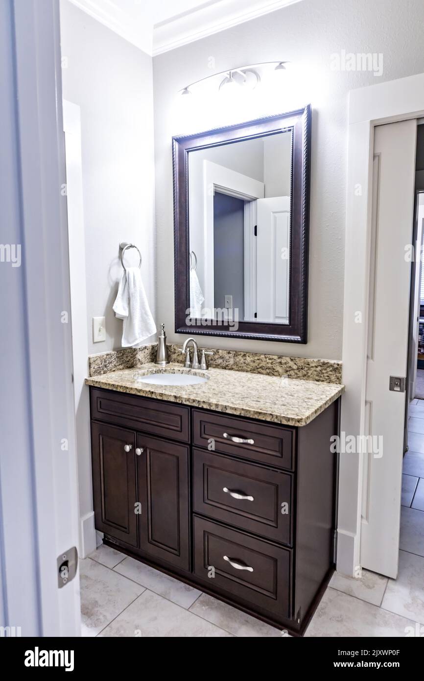 A modern new construction small guest bathroom with espresso cabinets, granite countertops, a tile floor and a mirror. Stock Photo