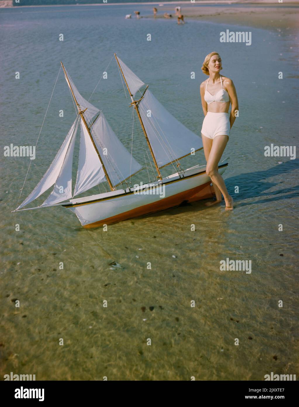 Portrait of Woman in Two-Piece Swimsuit standing on shore near Miniature Sailboat, Toni Frissell Collection, 1948 Stock Photo