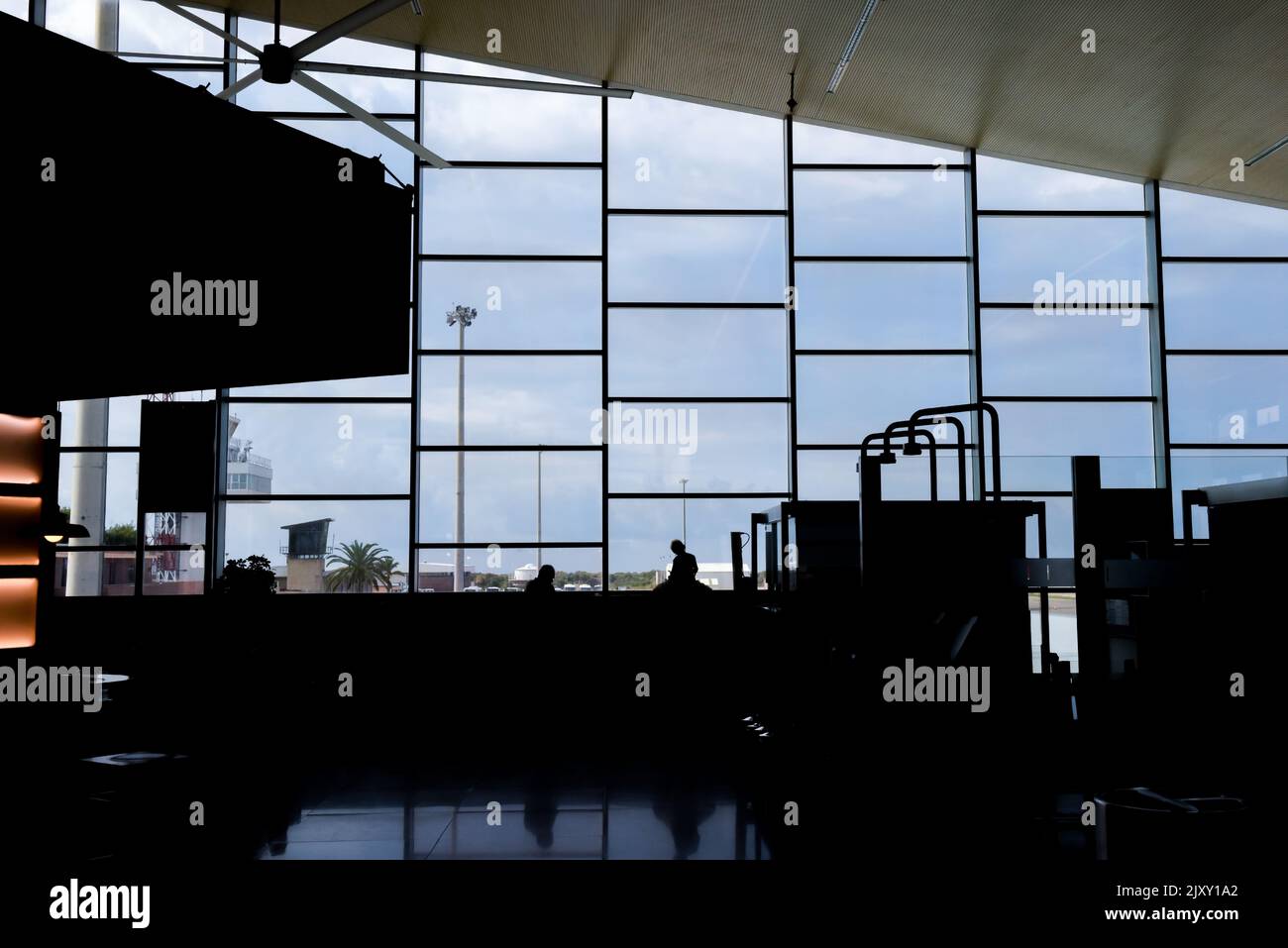 Airport departure lounge with people waiting for a flight looking out of a large glass window Stock Photo