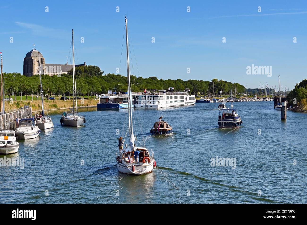 Veere, Netherlands - August 2022: Yacht and motorboats sailing towards the waterfront of the town with river cruise ships in the background Stock Photo