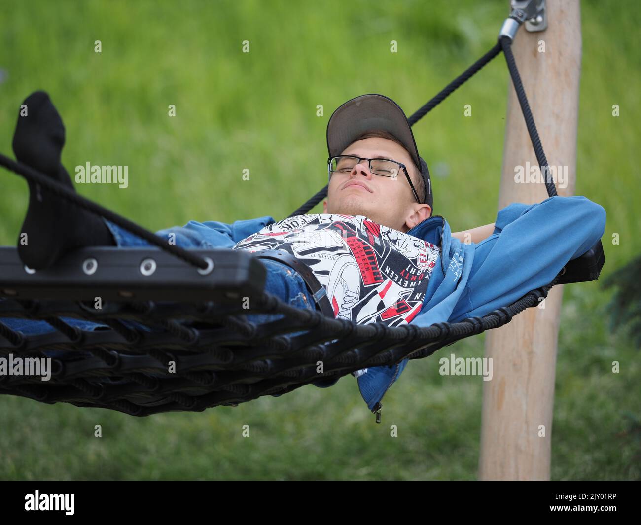 A young man is lying on a hammock in a park or garden outdoors. Stock Photo