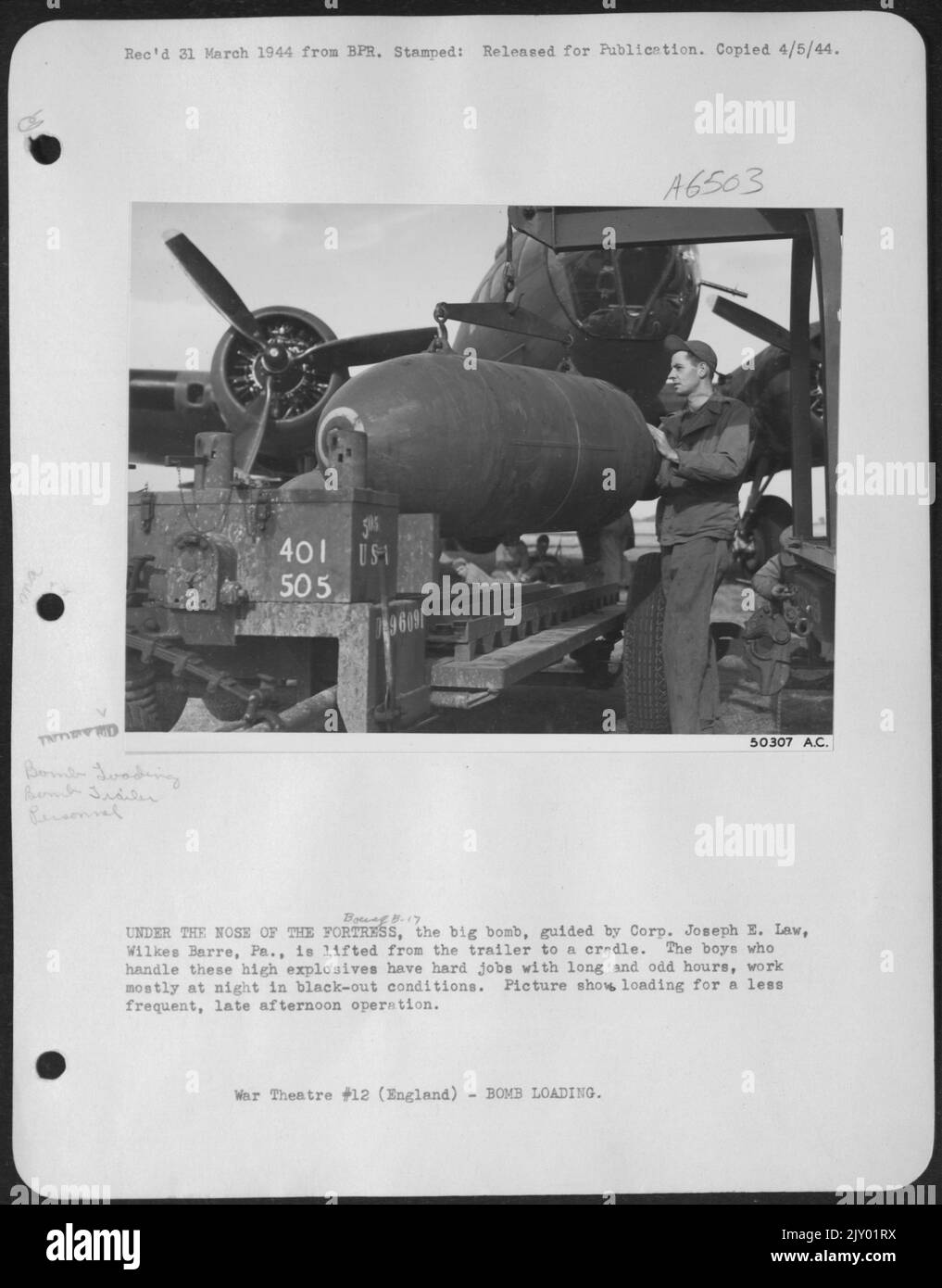 UNDER THE NOSE OF THE ofRTRESS, the big bomb, guided by Corp. Joseph E. Law, Wilkes Barre, Pa., is lifted from the trailer to a cradle. The boys who handle these high explosives have hard jobs with long and odd hours, work mostly at night in black Stock Photo