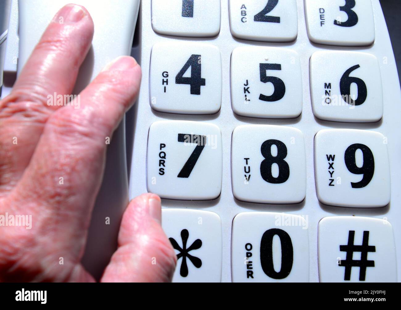 The hand of a senior or older man picks up the handset of a big button landline telephone which is aimed at elderly, disabled and sight impaired users Stock Photo