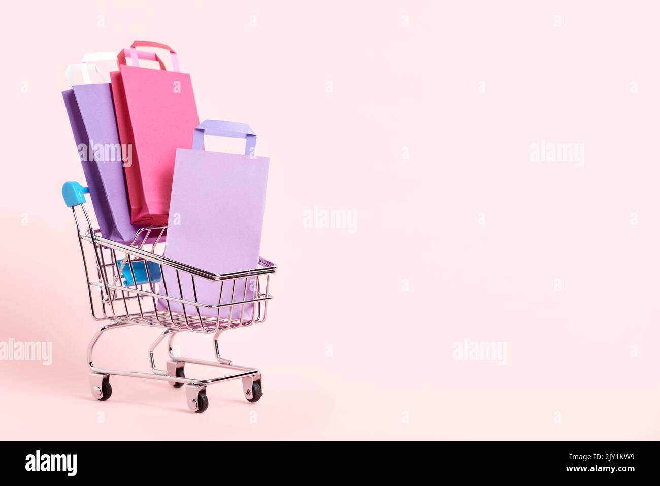 Shopping cart loaded with paper bags on a pastel pink background. Minimalist design with copy space. Concepts: market deals, seasonal sales and discou Stock Photo