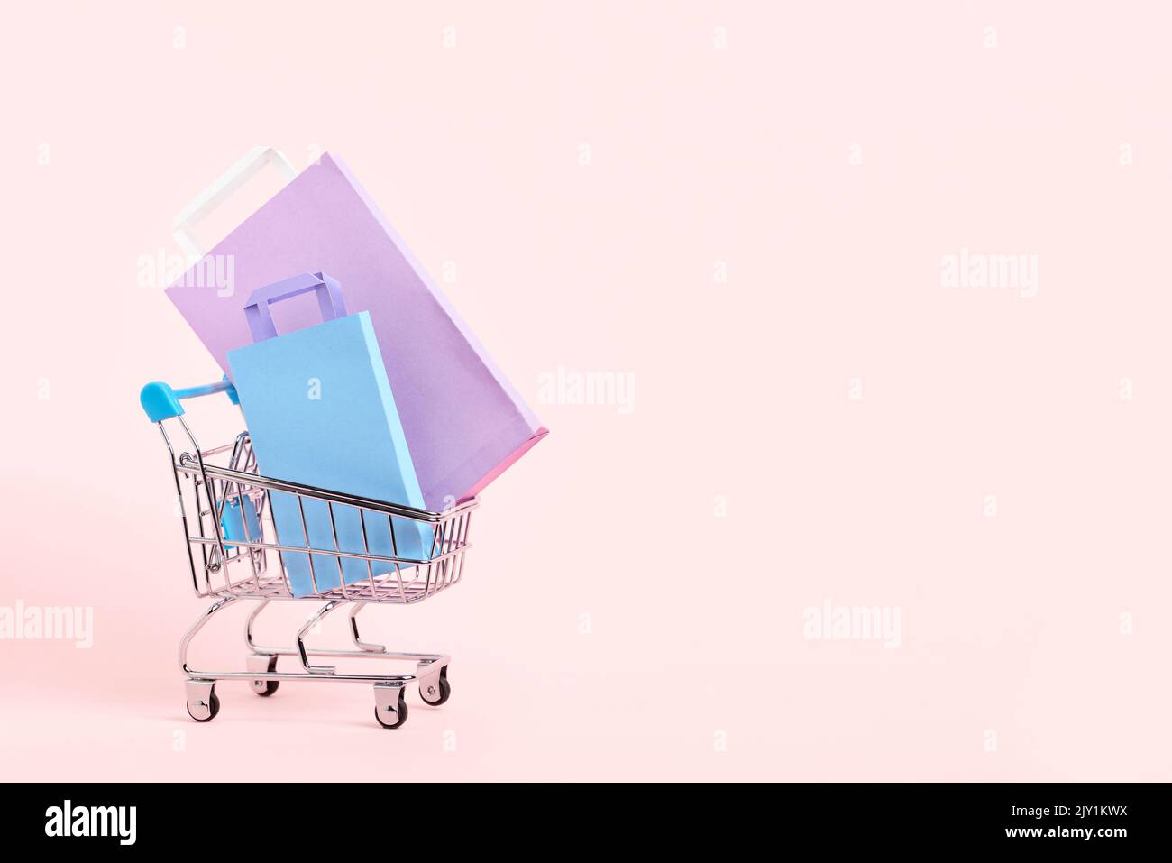 Shopping cart with purple, lilac and blue paper bags on a pastel pink background. Bright minimalist design with copy space. Concepts: market deals, se Stock Photo