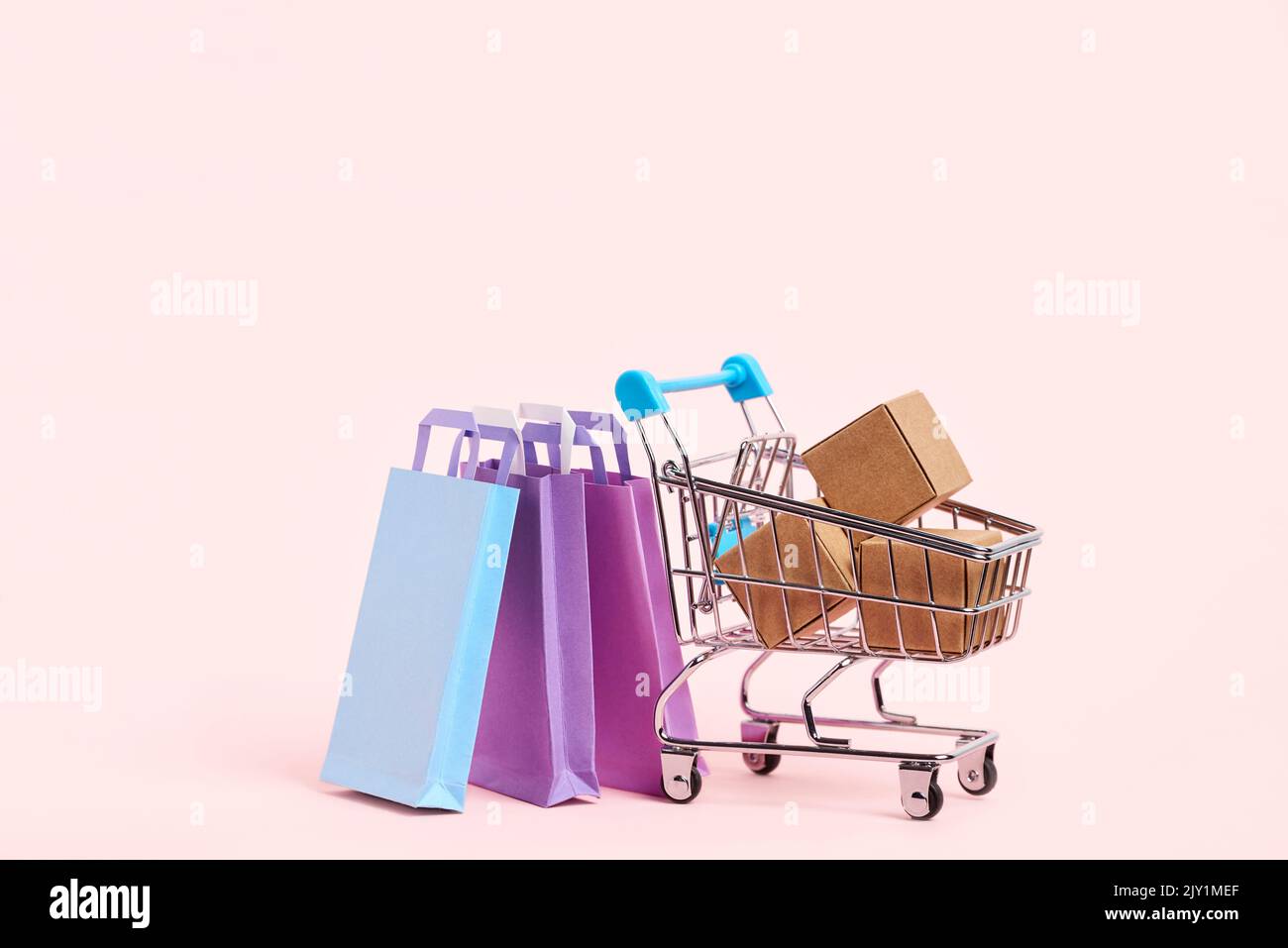 Shopping cart with cardboard boxes and paper bags on a pastel pink background. Simple design with copy space. Concepts: market sales, seasonal discoun Stock Photo