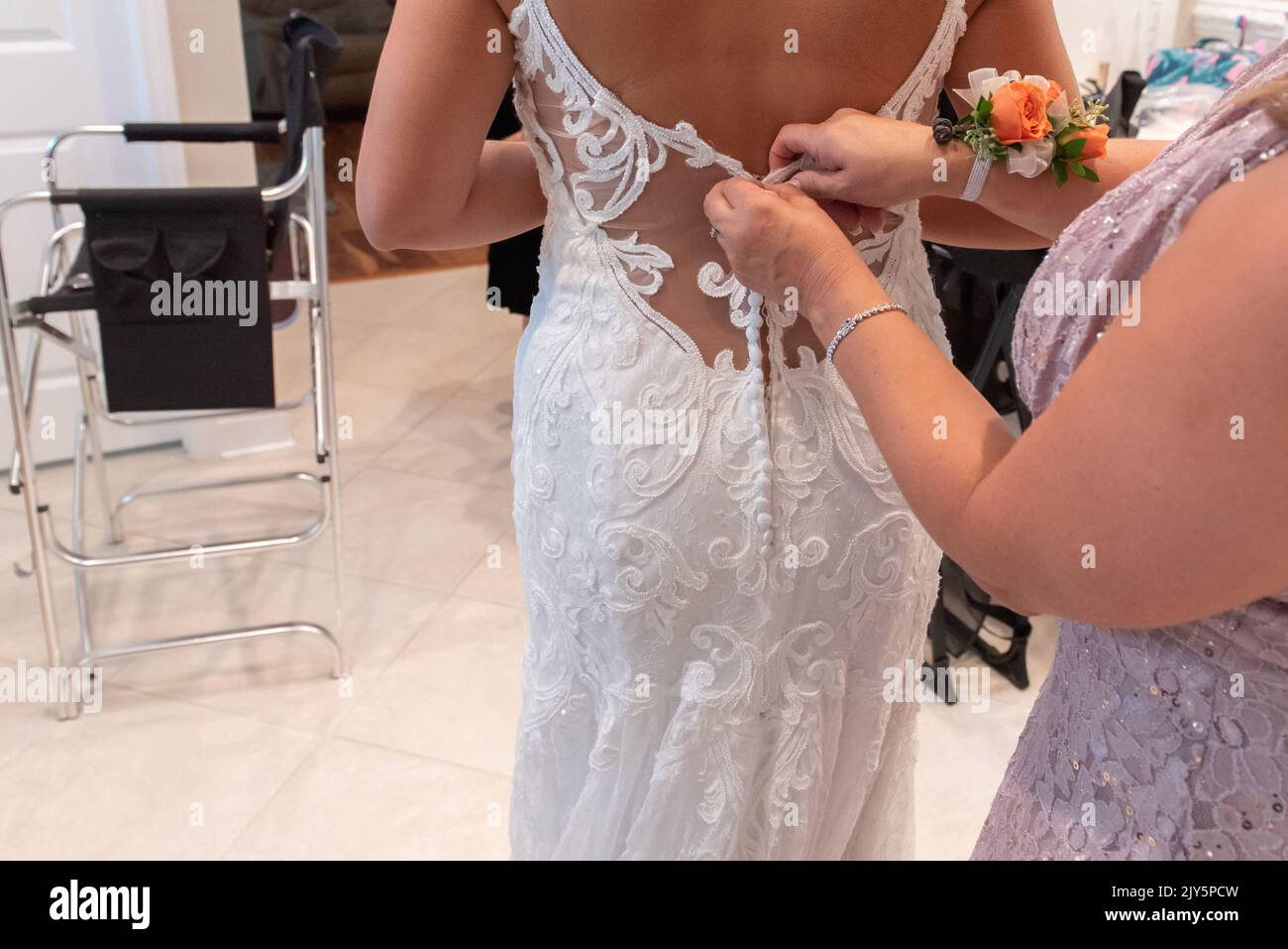 Bride receiving help buttoning the top buttons on her white laced wedding dress before the ceremony. Stock Photo