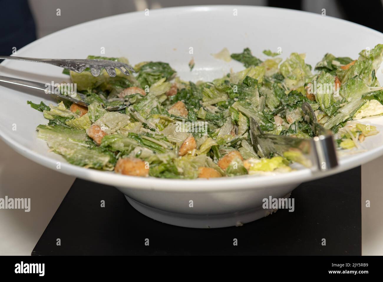 Large bowl of caesar sald has two pairs of tongs for the party guests