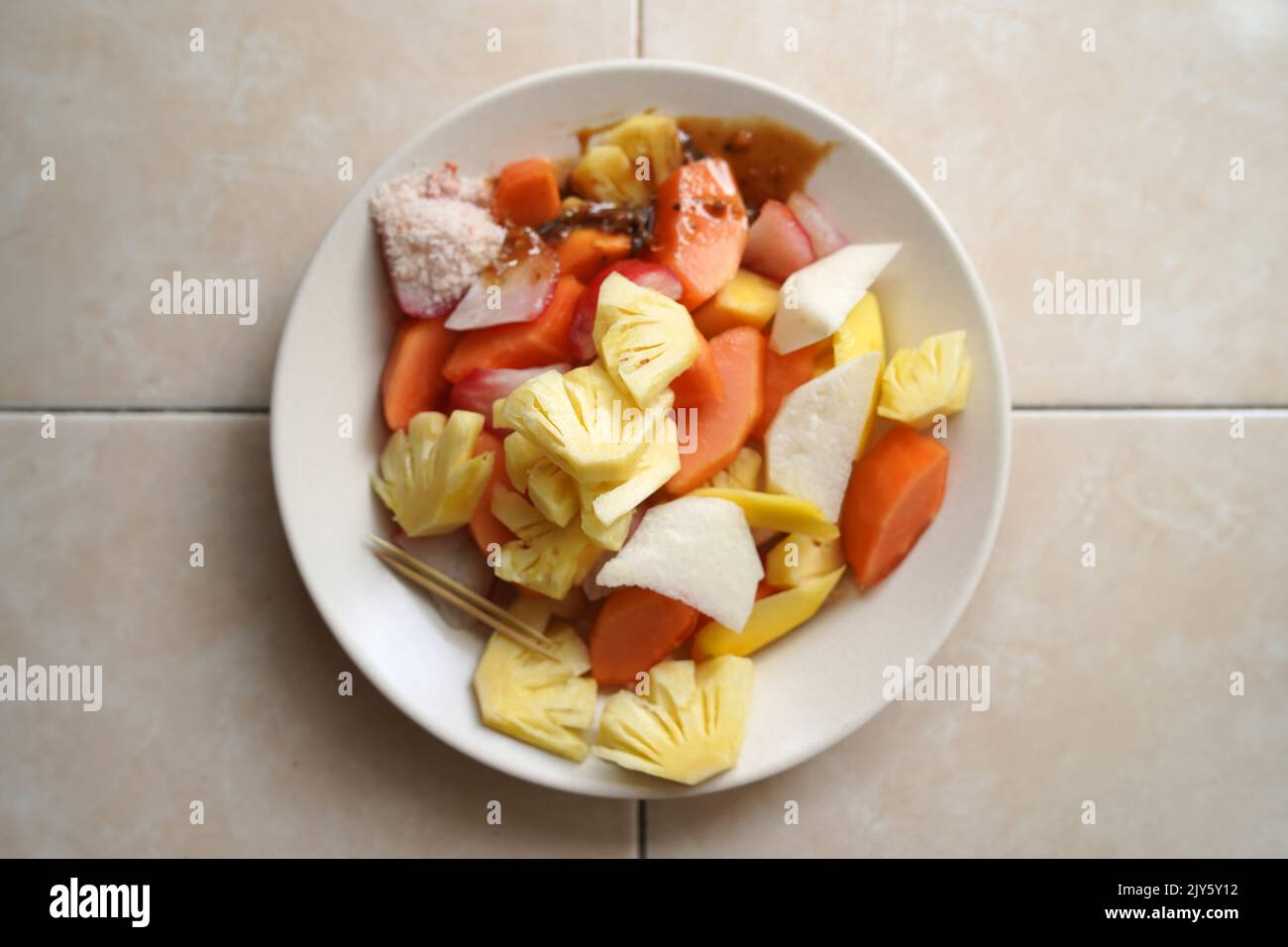 Rujak buah or indonesian fruit salad on white plate, served with spicy brown sugar sauce and ground peanuts. Stock Photo