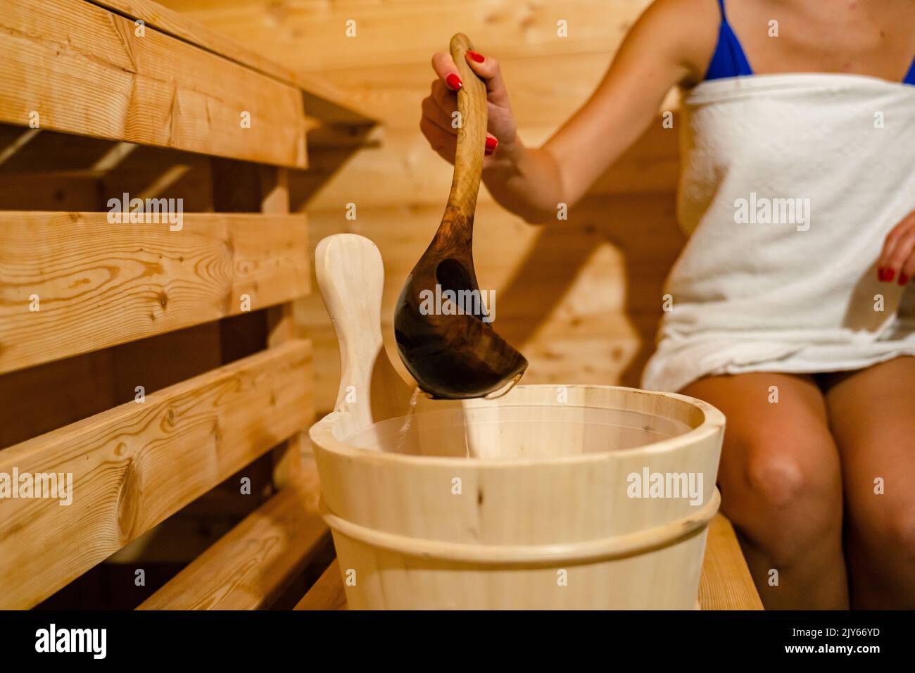 hand of unknown caucasian woman in sauna spa taking water from bucket with wooden spoon to pour on the hot stones Stock Photo