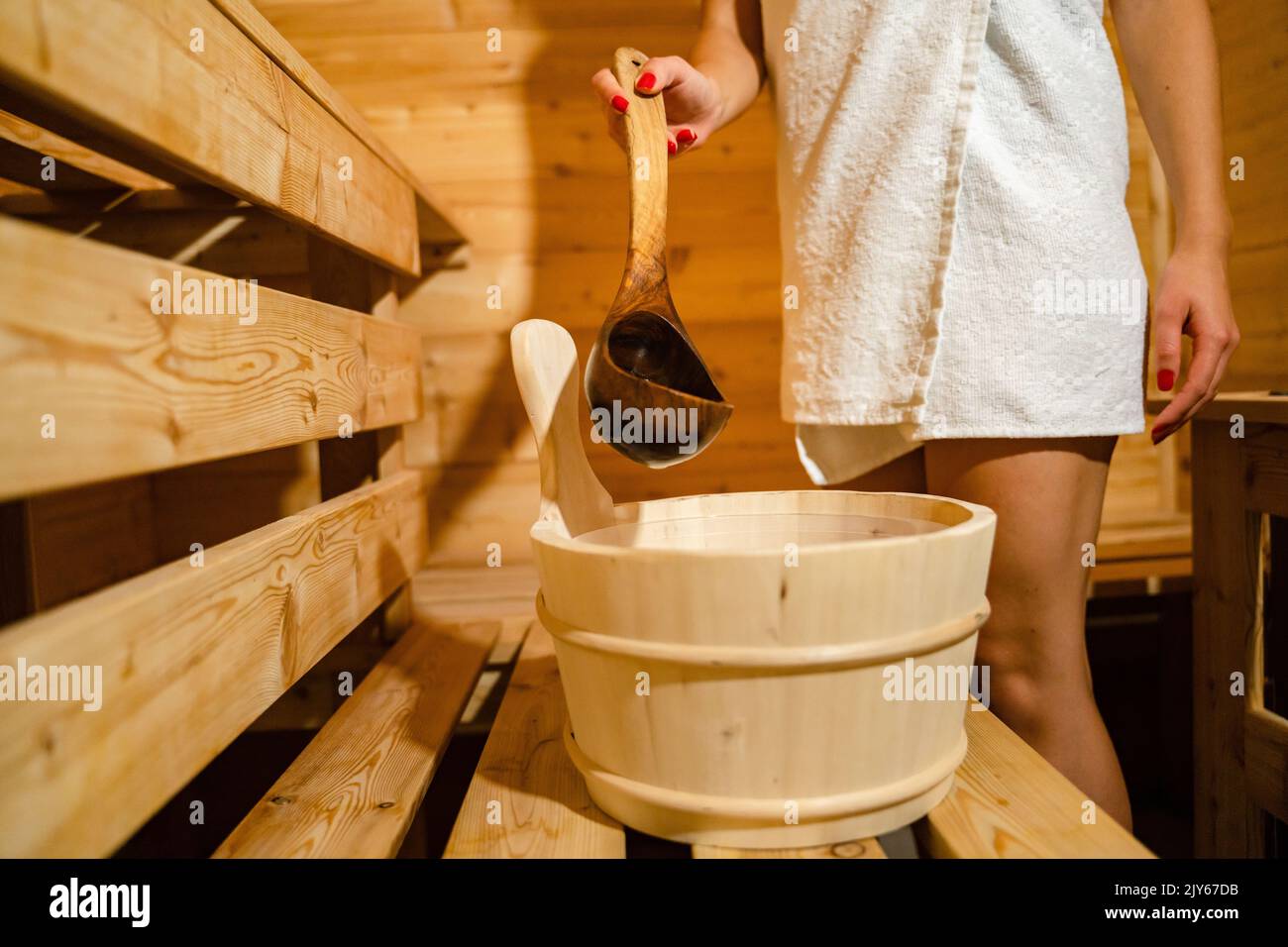 hand of unknown caucasian woman in sauna spa taking water from bucket with wooden spoon to pour on the hot stones Stock Photo
