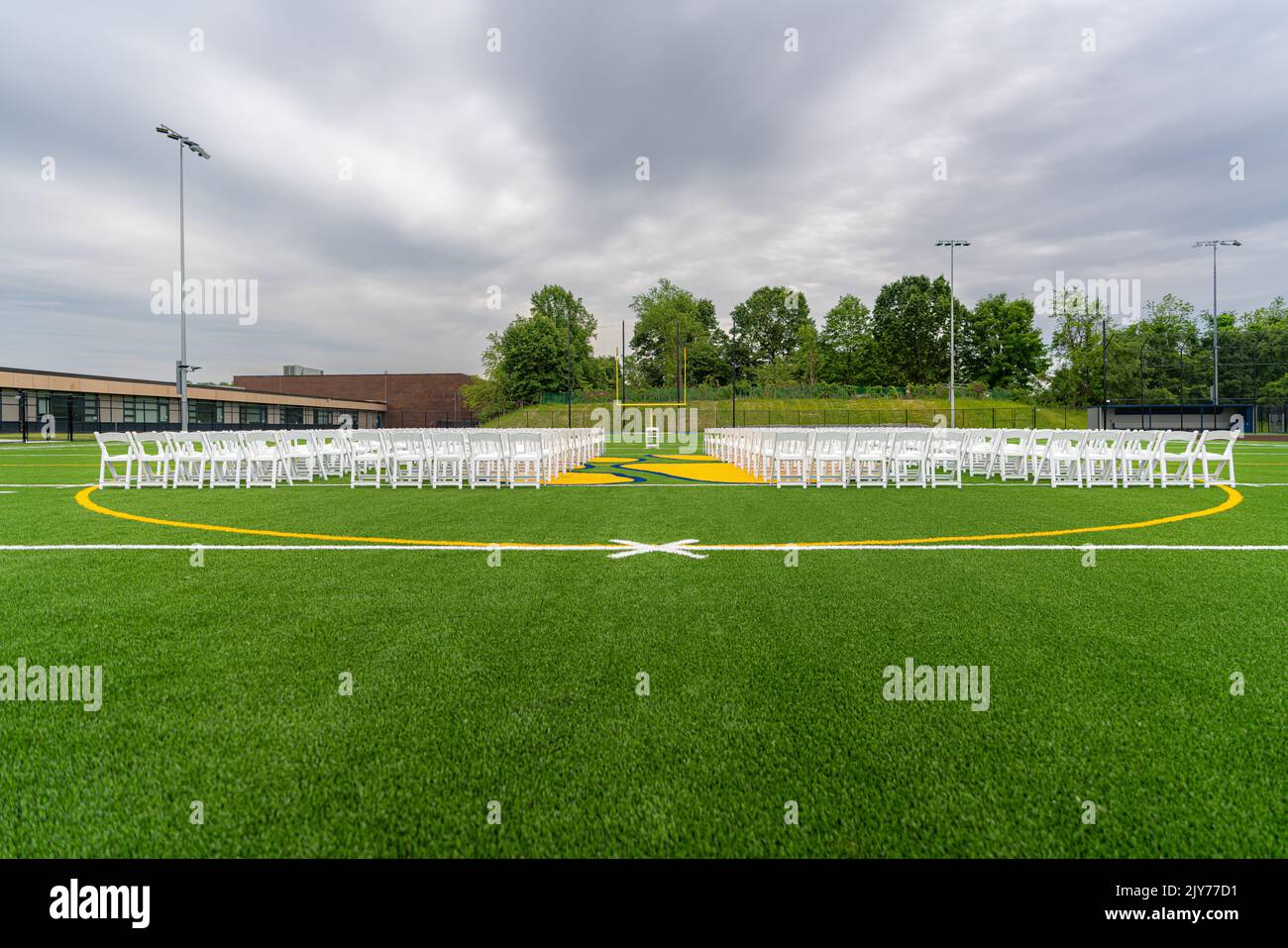 White chairs set-up in rows on a green synthetic turf athletic field for a high school graduation ceremony. Stock Photo