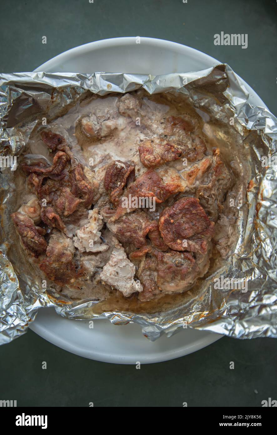 Baked juicy sliced meat is baked in foil. Spices and herbs are wrapped in foil. Cooking porks in the oven. Food for weekends and holidays, Copy spac Stock Photo