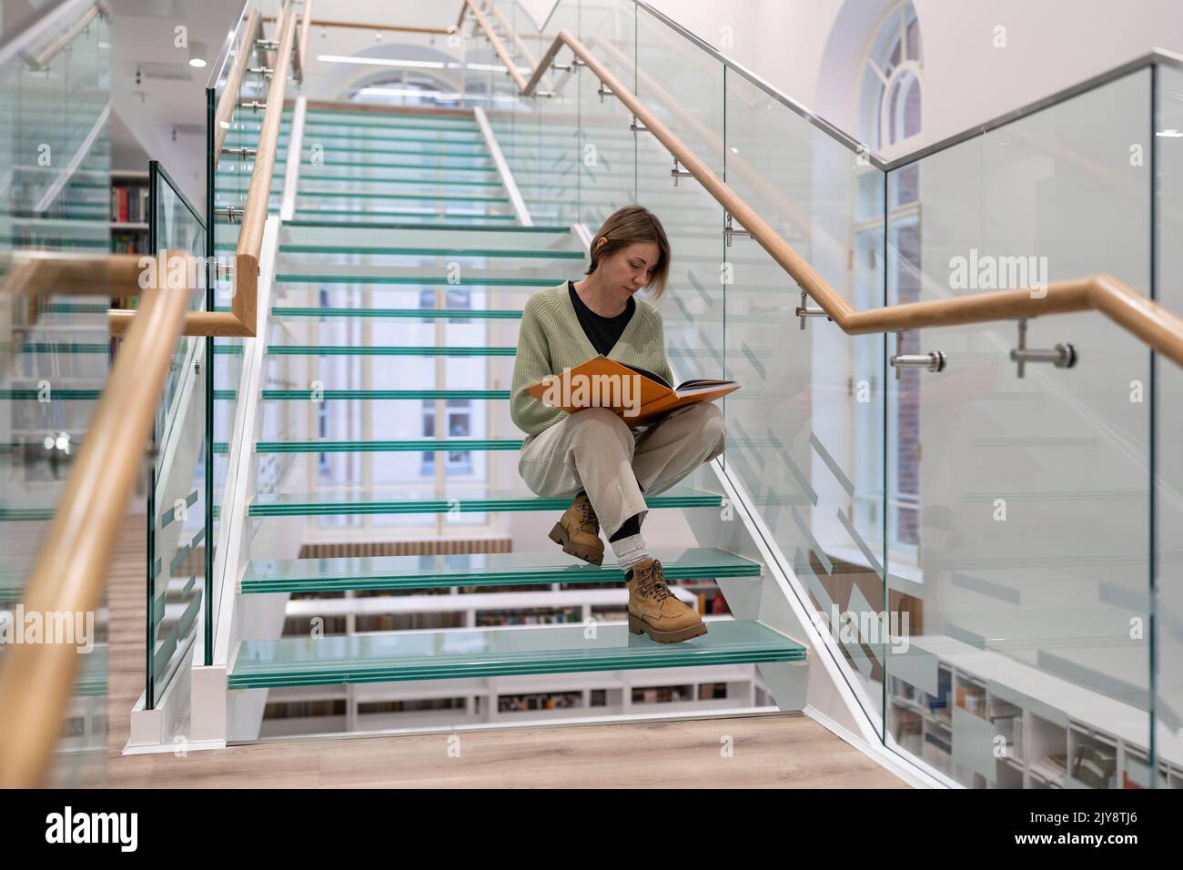 Step Reed R Curious female reader sits on modern glass stairs step reading favorite ...
