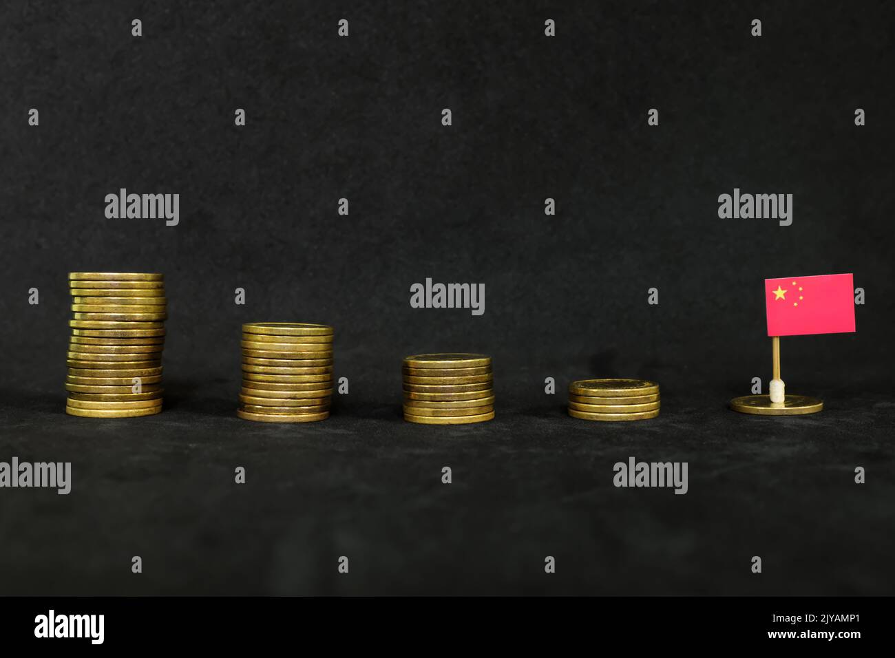 China economic recession, financial crisis and currency depreciation concept. Chinese flag in decreasing stack of coins in dark black background. Stock Photo