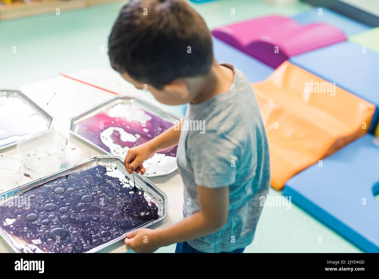 Sensory play for early brain development at nursery school. Toddler boy milk painting with his fingers, using nontoxic food coloring for colors, milk and trays. Creative kids activity for fine motor and gross motor skills development. High quality photo Stock Photo