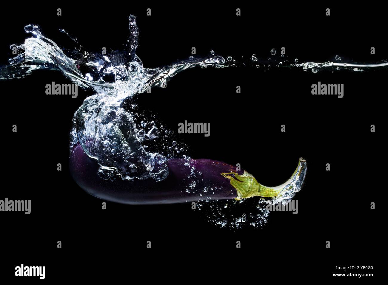 Fresh whole eggplant dropped in water with splashes on black Stock