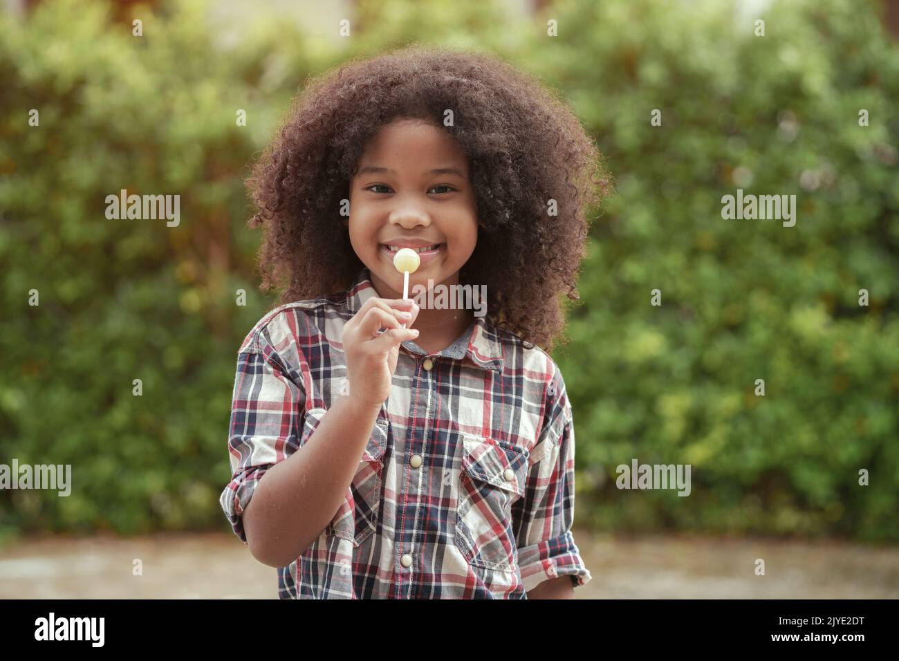 Happy African-American kid girl with a lollipop in her hands in the garden or outdoors. Stock Photo