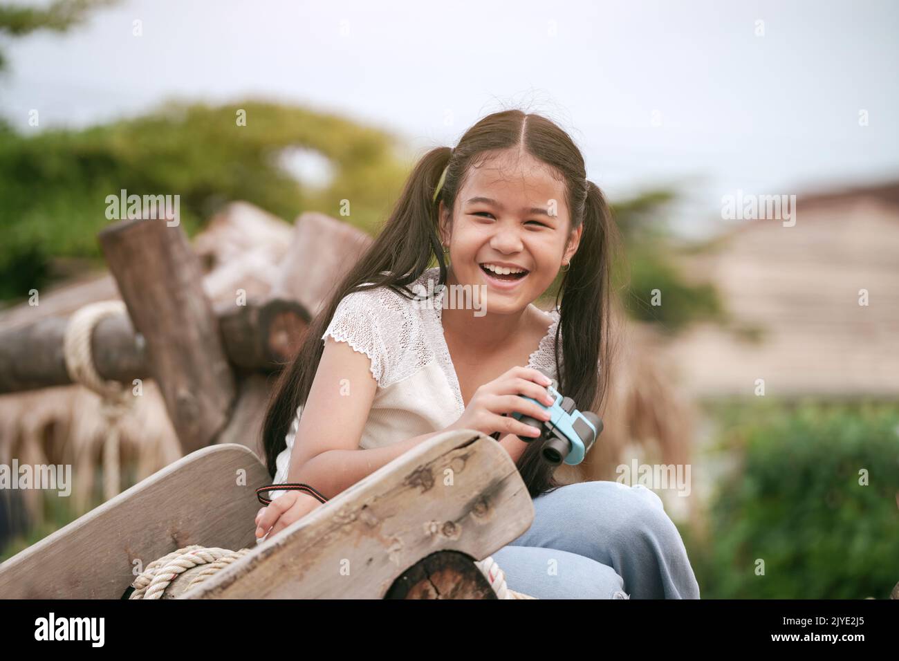 Happy girl kid is laughing and holding binoculars in her hands in the playground. Stock Photo