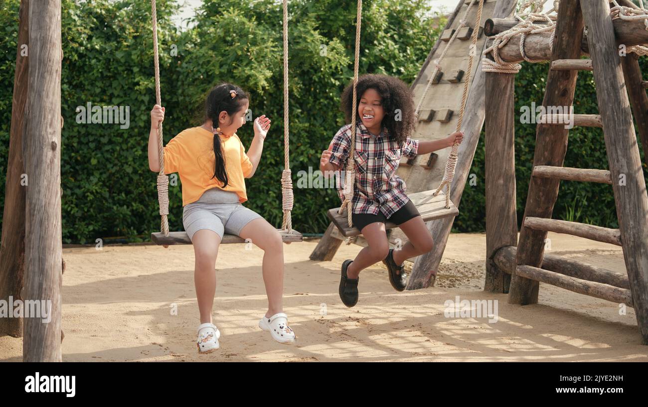 Two kids girl are playing on the swing in the outdoor playground. Stock Photo