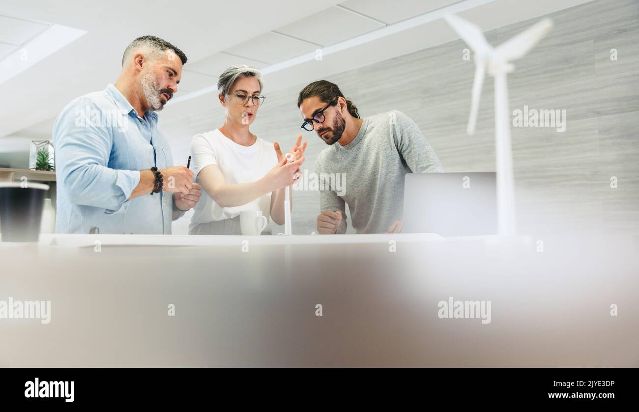 Innovative designers working with 3D wind turbine models in a modern office. Group of creative businesspeople having a discussion while working on a r Stock Photo