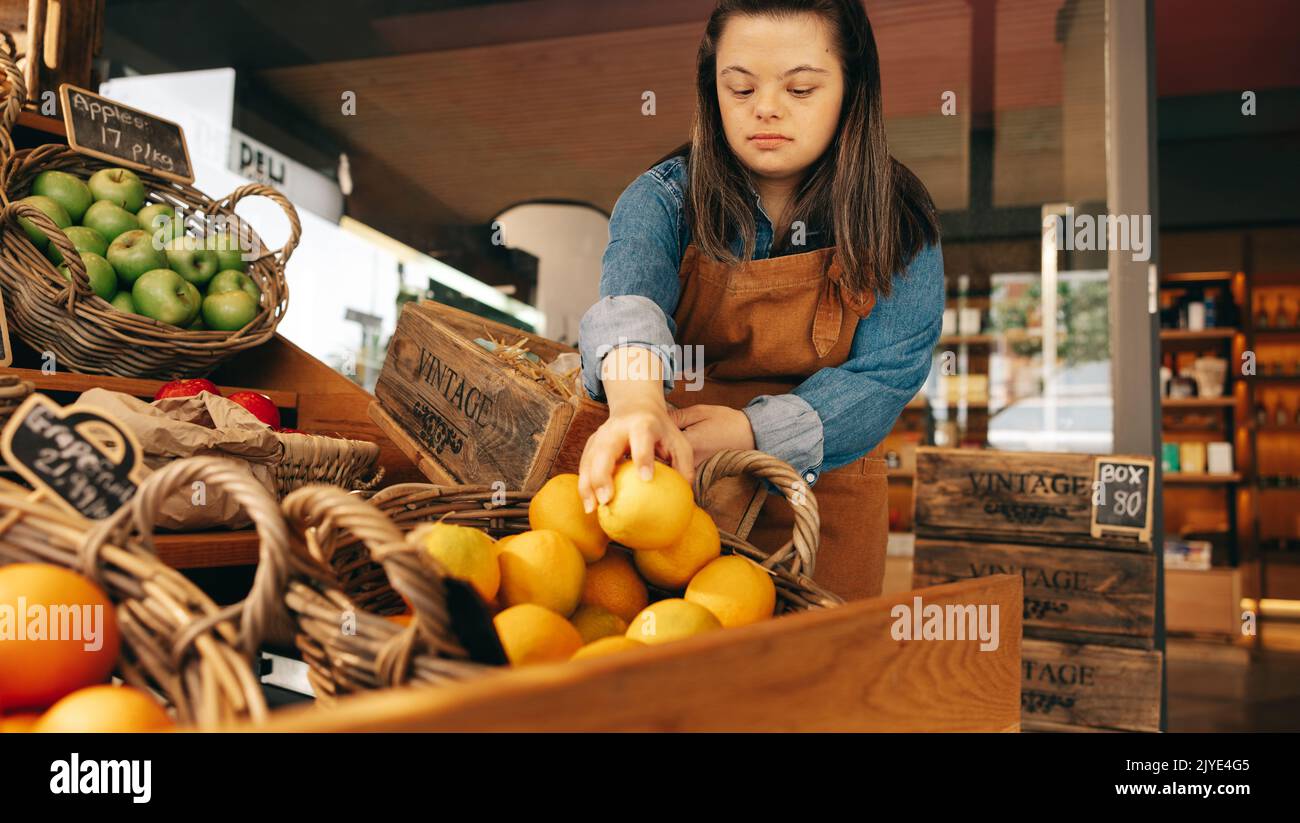 Grocery store employee with Down syndrome restocking fresh fruits in the vegetable section of a grocery store. Empowered woman with an intellectual di Stock Photo