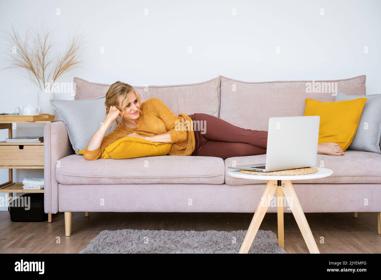 Business freelance woman working on laptops, checking social media, lying on sofa and watching movie while relaxing in living room at home. Lifestyle at home caucasian girl freelancer concept. Stock Photo