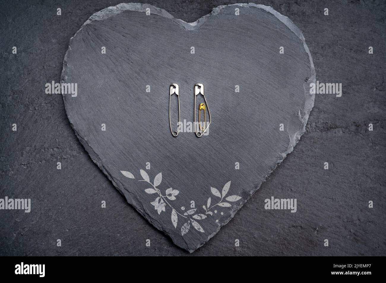 Safety pins on a heart made of slate symbolize pregnancy and family planning Stock Photo