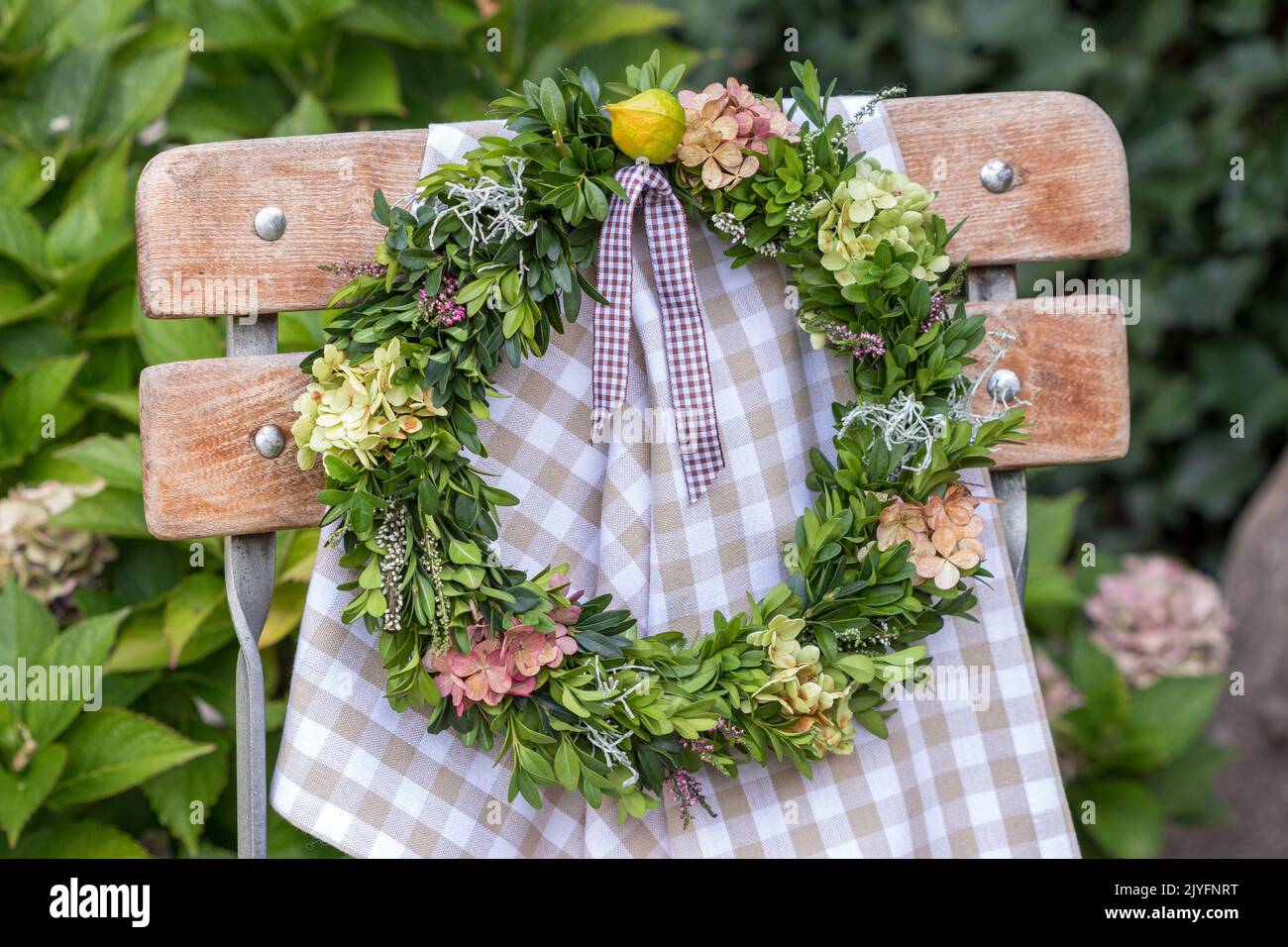wreath of hydrangea flowers and box tree branches hanging on garten chair Stock Photo