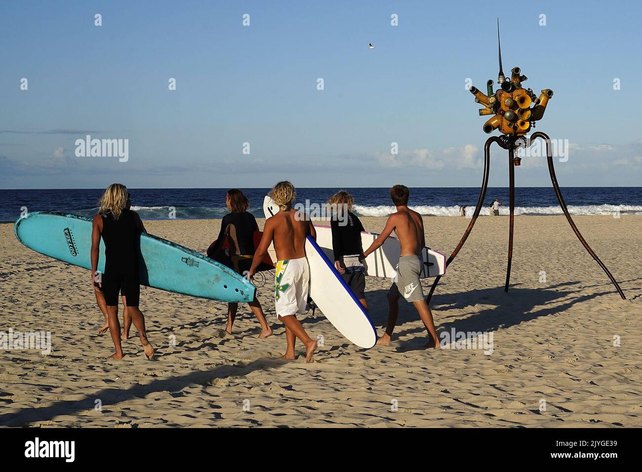 Surfers walk past an art exhibit as part of the Swell Sculpture