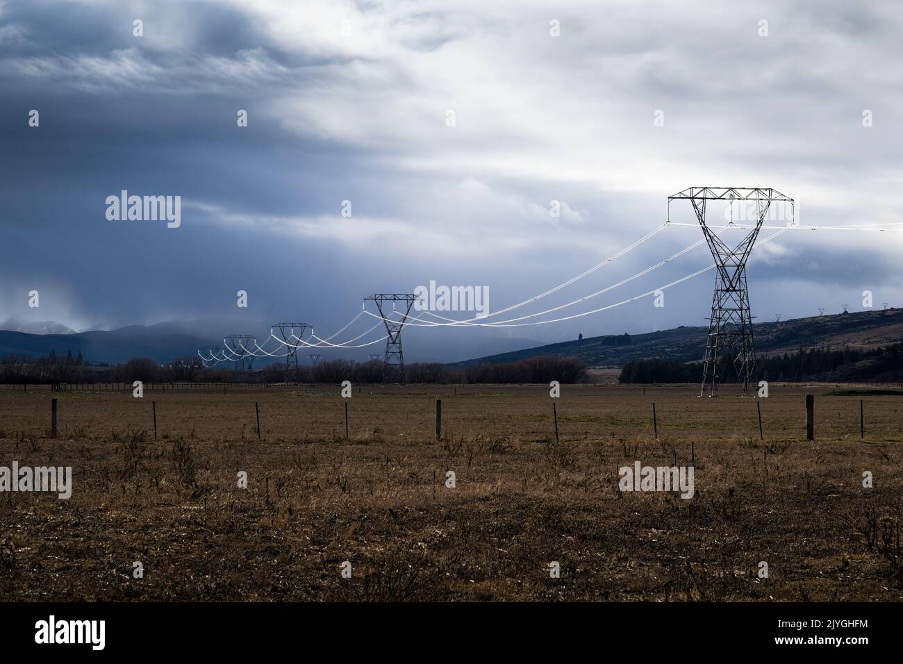 Power lines lit up by the sunlight coming through dark clouds, Central Otago, South Island. Stock Photo