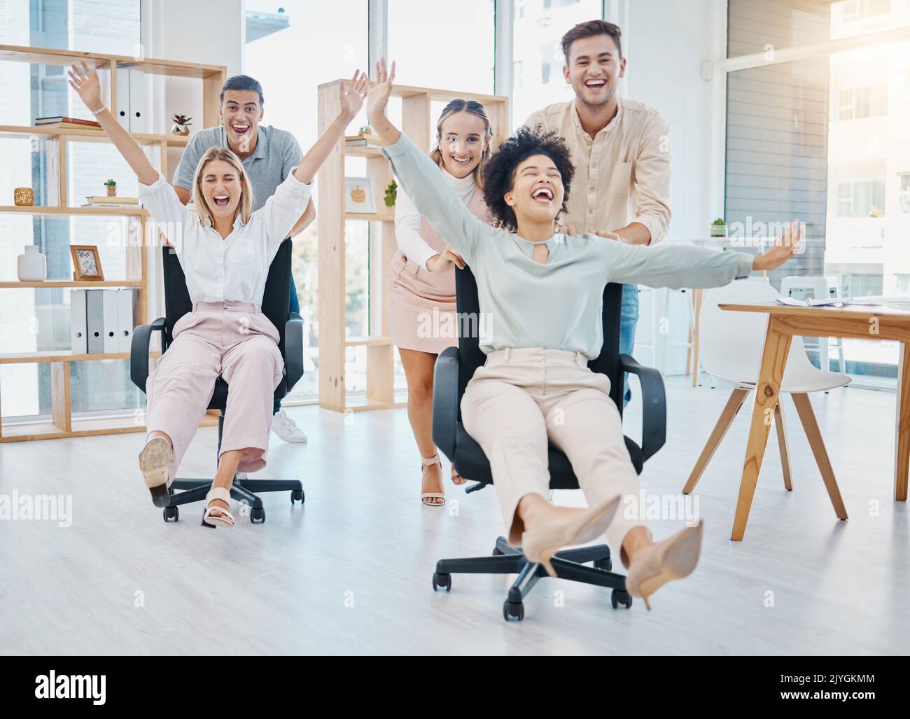 Happy business people doing office games with chair at work, celebration of success and freedom at startup company and crazy teamwork at job. Comic Stock Photo