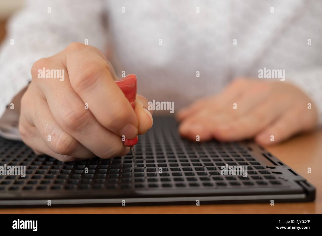 A woman uses a special stencil and stylus to write a letter in braille