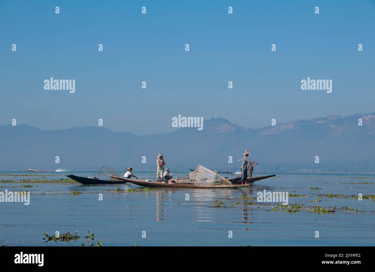 Burma / Myanmar: Leg rowing Intha fishermen on Inle Lake, Shan State. Inle Lake is a freshwater lake located in Shan State. It is the second largest lake in Myanmar and one of the highest at an altitude of 2,900 feet (880 m). The people of Inle Lake (called Intha), some 70,000 of them, live in four towns bordering the lake, in numerous small villages along the lake's shores, and on the lake itself. The population consists predominantly of Intha, with a mix of other Shan, Taungyo, Pa-O (Taungthu), Danu, Kayah, Danaw and Bamar ethnicities. Stock Photo