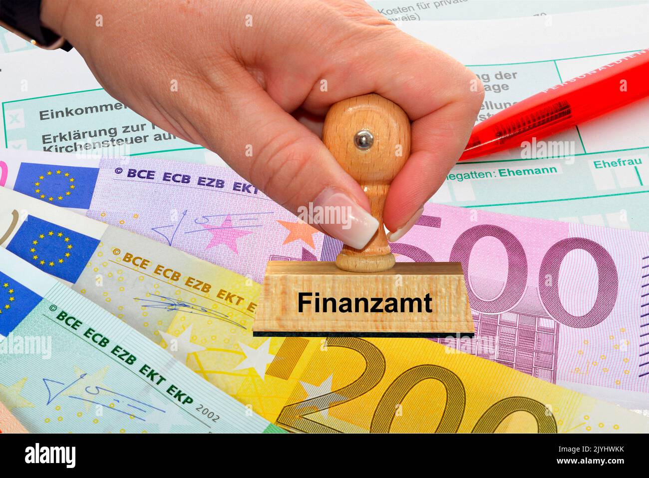 woman's hand with stamp lettering, Finanzamt, taxation office, Euro bills an pencil in the backgound, Germany Stock Photo