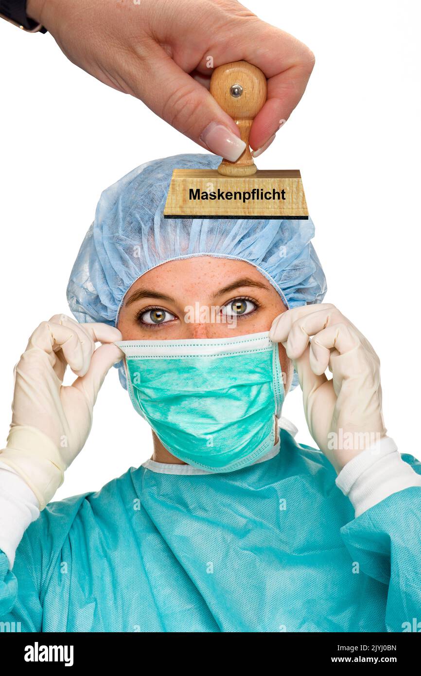 woman's hand with stamp lettering Maskenpflicht, mask mandate, hospital nurse with mask in the background, Germany Stock Photo